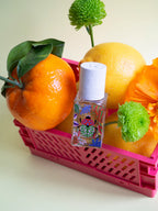 Nature Insolente Eau de Parfum – colorful glass bottle with white spray cap, pink crate, citrus fruits – perfume