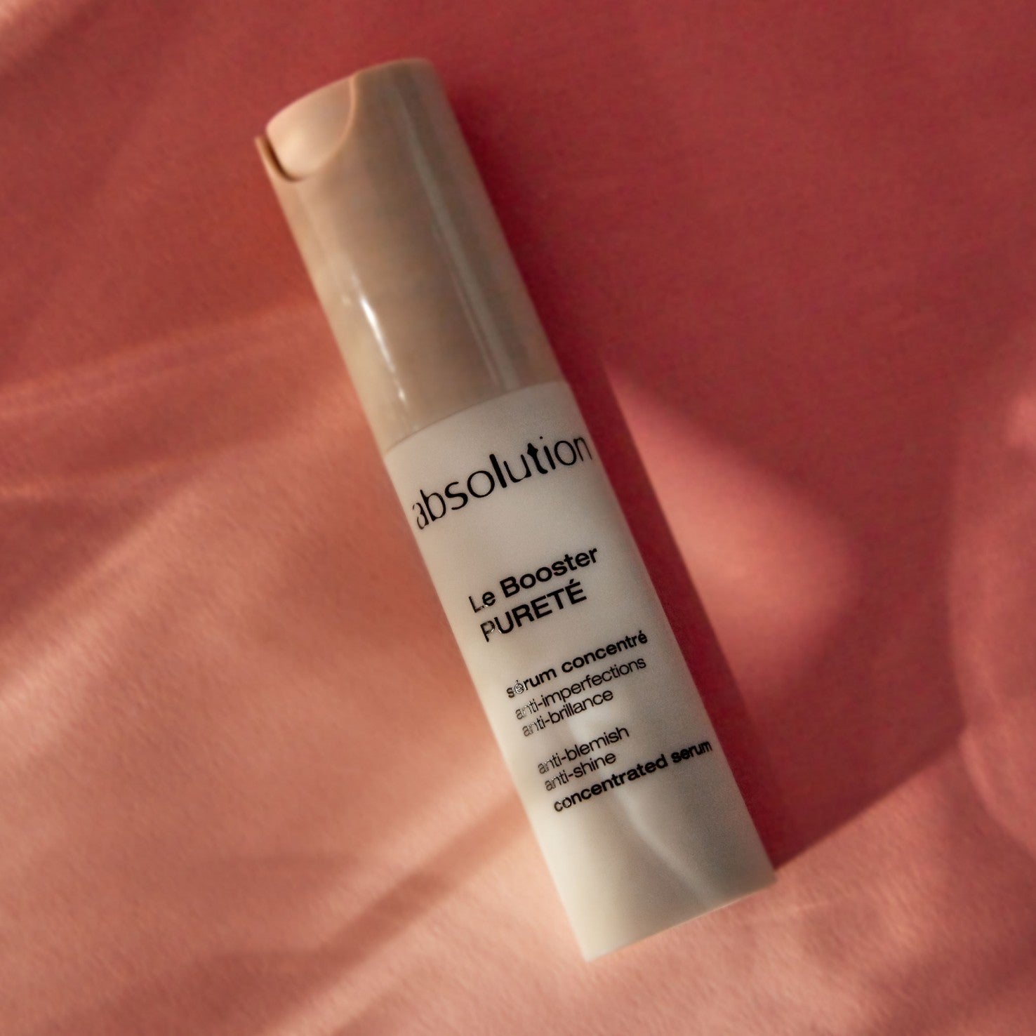 Absolution Le Booster Pureté in einer weißen Flasche mit beigem Verschluss auf rosa Hintergrund, Hautpflege-Serum