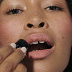 Lip to Cheek Blush – black stick, applied to lips, dark background – face makeup