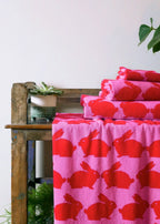 Kissing Rabbits Organic Cotton Hand Towel – pink with red rabbits, on wooden bench, white background – bath textiles