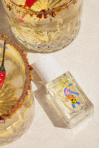 Ukhu Pacha Eau de Parfum – clear glass bottle with colorful label, white cork stopper, cream background – perfume