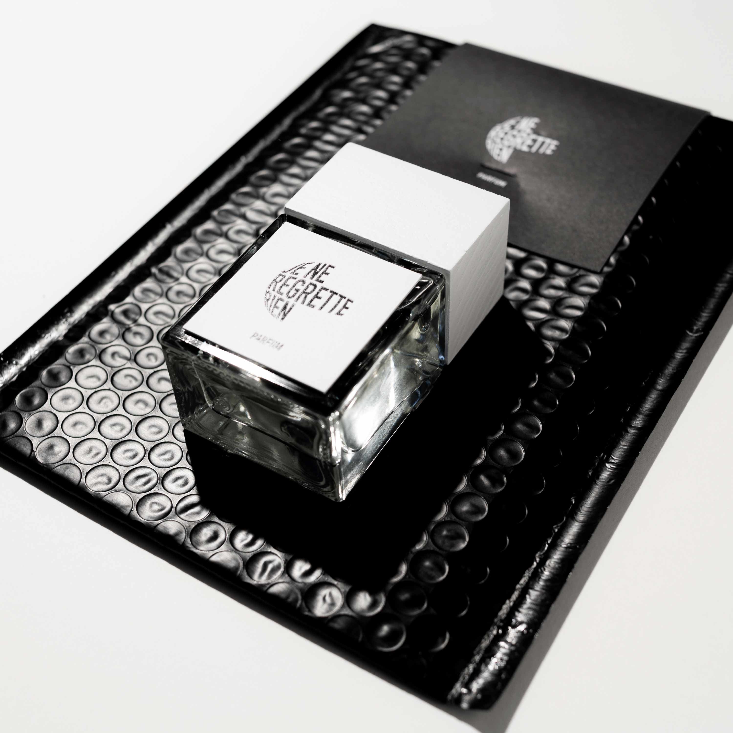 Je Ne Regrette Rien Parfum – quadratische Glasflasche mit weißem Deckel, schwarzer Hintergrund – Parfüm