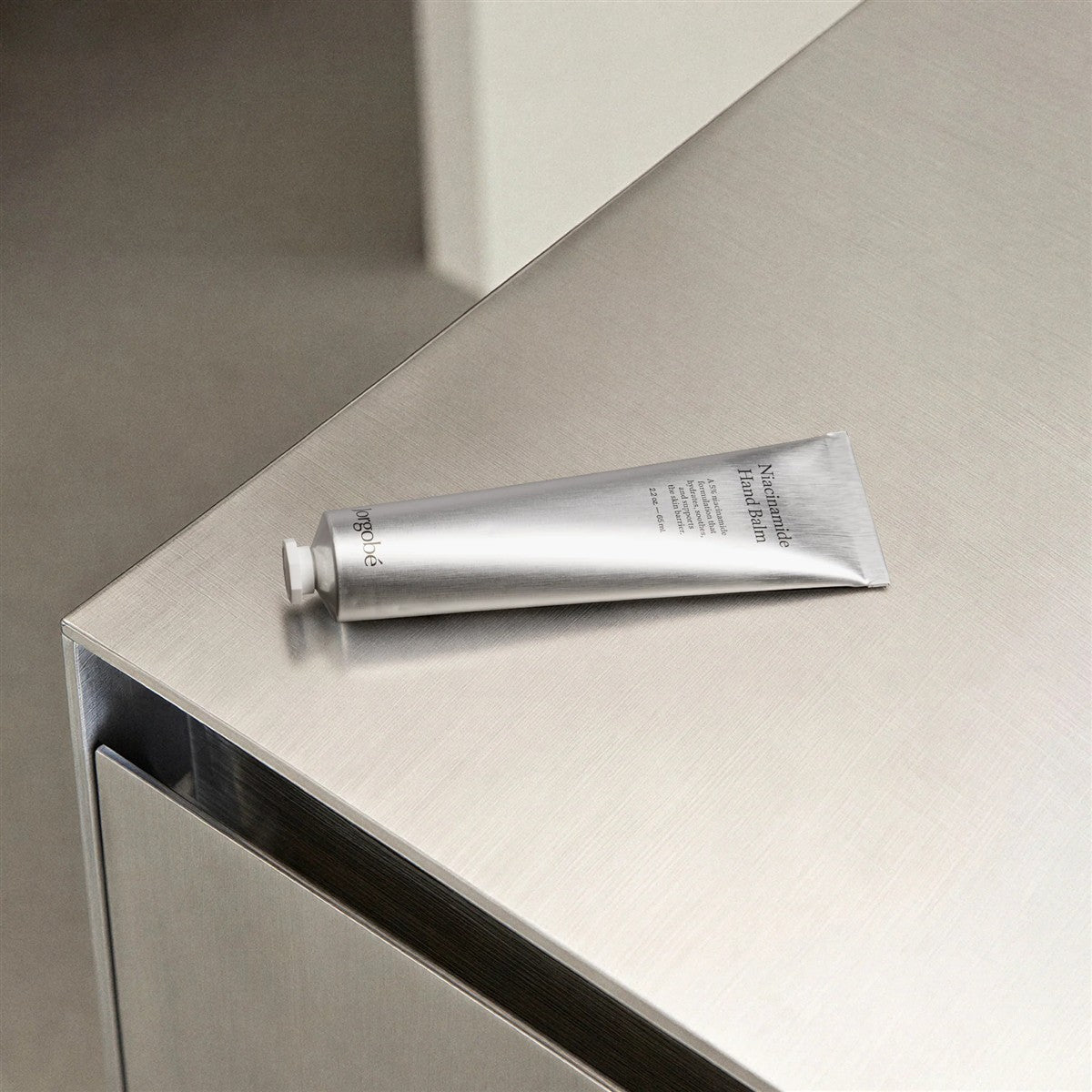 Orgobe Niacinamid Handbalsam – silberne Tube 60ml, weißer Verschluss, metallischer Hintergrund – Hautpflege