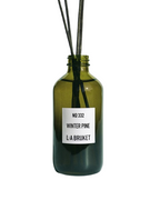 L:A Bruket No. 332 Winter Pine – grüne Glasflasche mit Rattanstäbchen, weißem Etikett und weißem Hintergrund – Raumduft