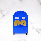 Soft Curve Earrings – gold wavy drop earrings on blue display, marble background – jewelry