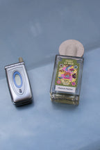 Maison Matine Faire Le Mur Eau de Parfum – clear glass bottle with colorful label, round stone cap, blue background – perfume