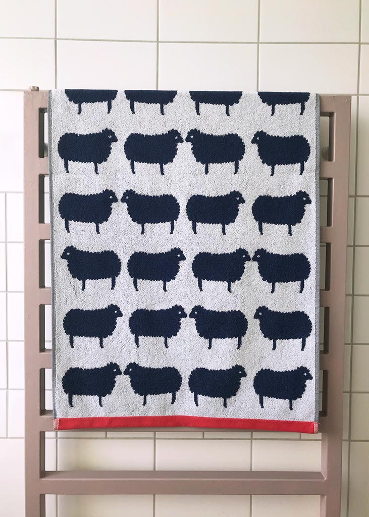 Sheep Organic Cotton Badelaken mit Schaf-Muster, grau-schwarz, roter Saum, auf Heizkörper – Strandtuch