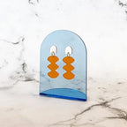 Spectral Orange Earrings – orange geometric shapes on blue acrylic holder, marble background – jewelry