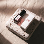Peau Secrète Perfume Oil – dark glass bottle with black cap, white box on porous stone – perfume