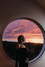 No product visible: Silhouette of a woman in front of a round window at sunset, skin care context.