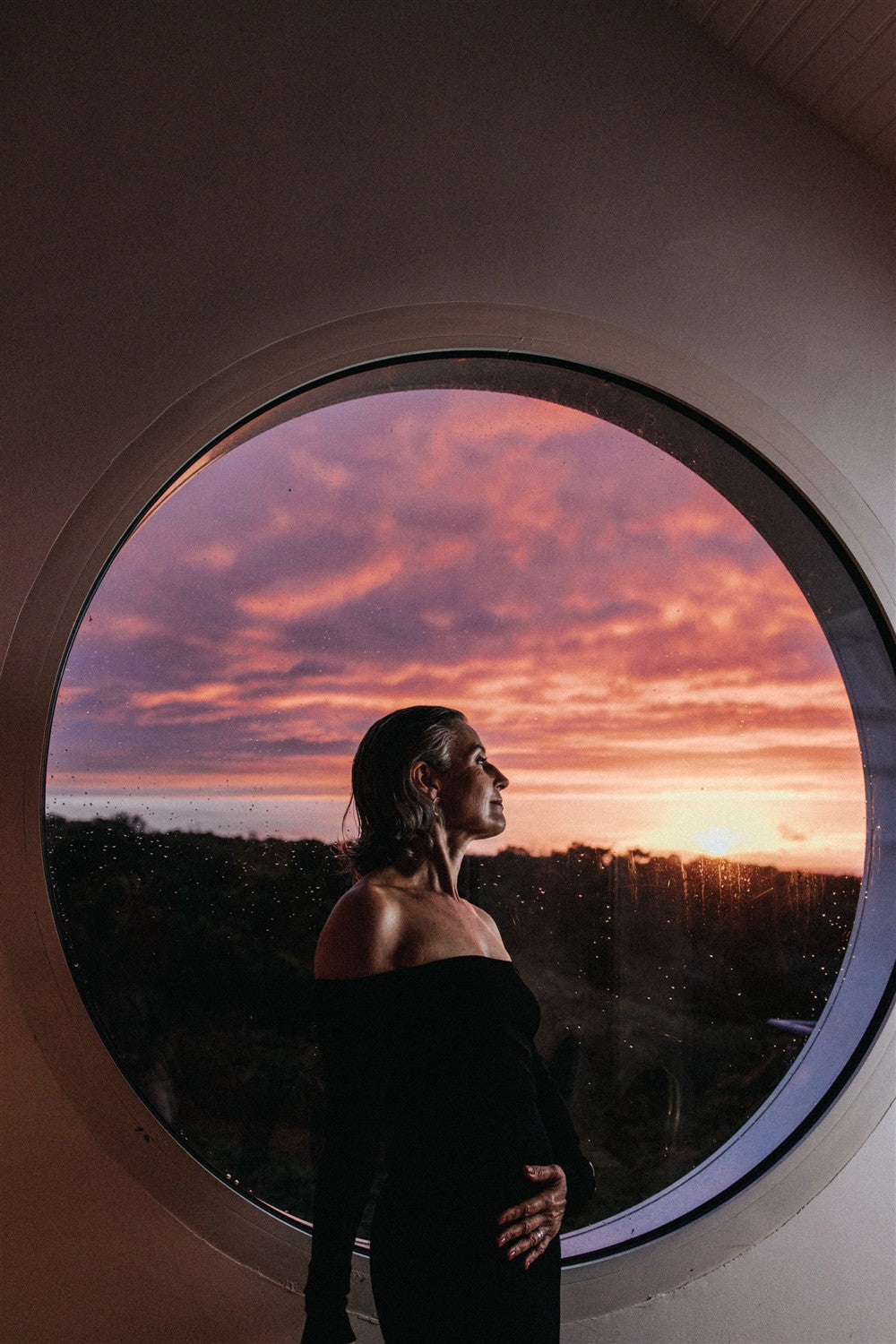 No product visible: Silhouette of a woman in front of a round window at sunset, skin care context.
