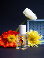 Lost in Translation Eau de Parfum – quadratische Glasflasche mit weißem Sprühkopf, dunklem Hintergrund, umgeben von Blumen – Parfüm