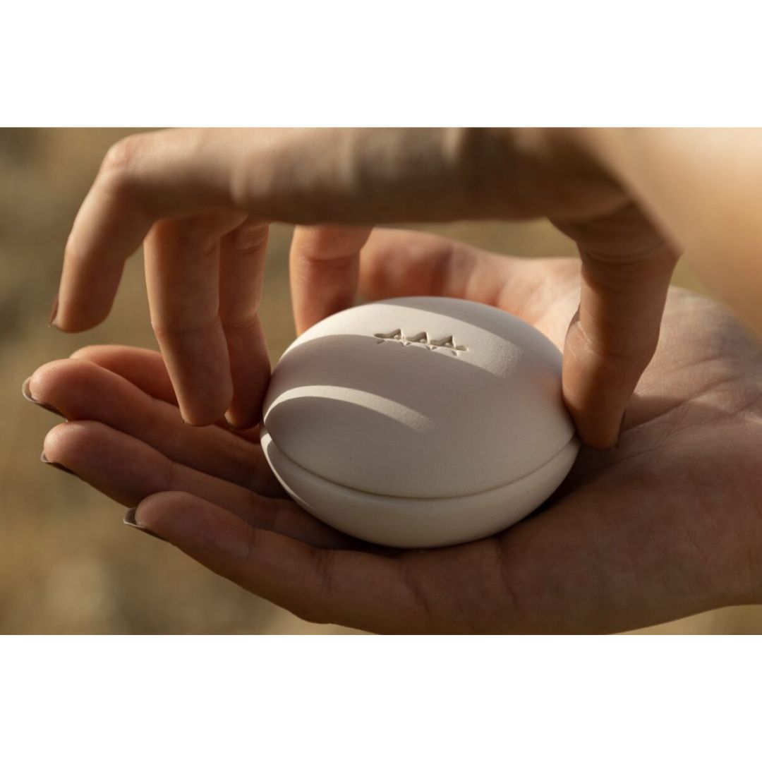 Scia – cream-colored round container, held in hands, blurred natural background – skin care