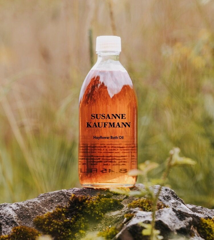 Susanne Kaufmann Hayflower Bath Oil in einer gläsernen Flasche mit weißem Verschluss vor Naturhintergrund, Körperpflege, Moodbild