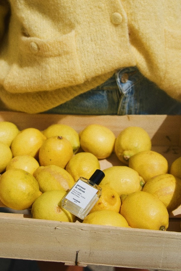 Presser Le Citron Roll-on Parfümöl in einer klaren Glasflasche mit schwarzem Verschluss zwischen Zitronen, Duftöl