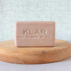 KLAR Cocoa Butter Soap – pink solid bar, on wooden plate, light gray background – skin care