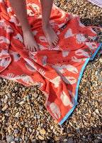 Lobster Organic Cotton Beach Towel – vibrant orange with white lobster print, blue border, on pebble beach – beach accessories