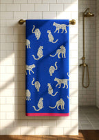 Snow Leopard Bio-Baumwollhandtuch – tiefblau mit Leopardenmuster, rosafarbener Saum, hängend an Messinghalter – Badezimmer-Accessoire
