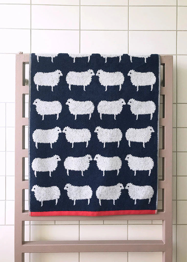 Sheep Organic Cotton Waschlappen – dunkelblau mit weißen Schafen, roter Saum, auf Heizkörper – Gesichtspflege