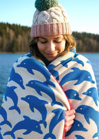 Jumping Dolphins organic cotton beach towel in blue and beige, worn by a woman, bath towel.