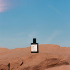 Sea, Sud & Sun Versatile Parfum in einer dunkelblauen Flasche mit schwarzem Verschluss auf rötlichem Fels, Parfüm