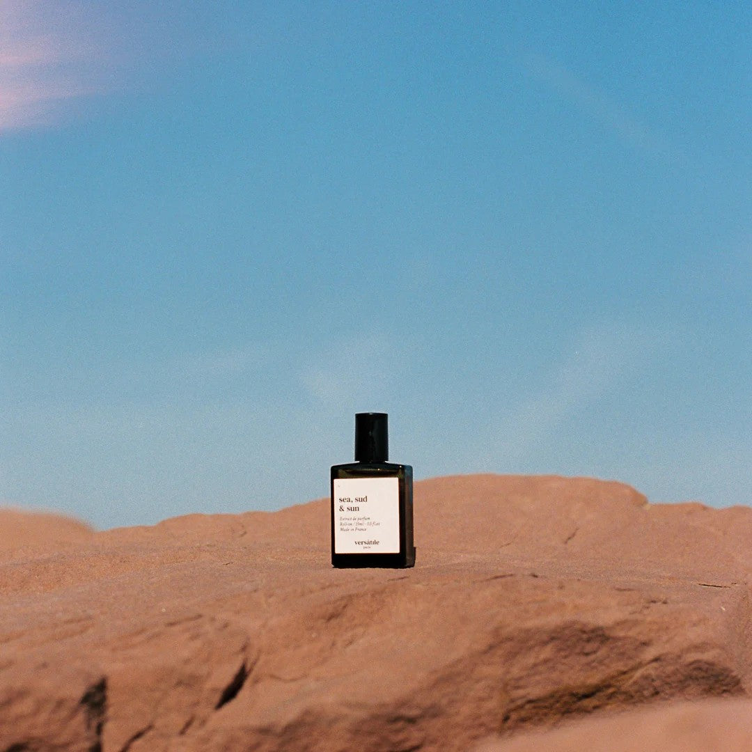 Sea, Sud & Sun Versatile Parfum in einer dunkelblauen Flasche mit schwarzem Verschluss auf rötlichem Fels, Parfüm