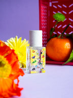 Poom Poom Eau de Parfum – square glass bottle with colorful motifs, white spray cap, purple background – perfume
