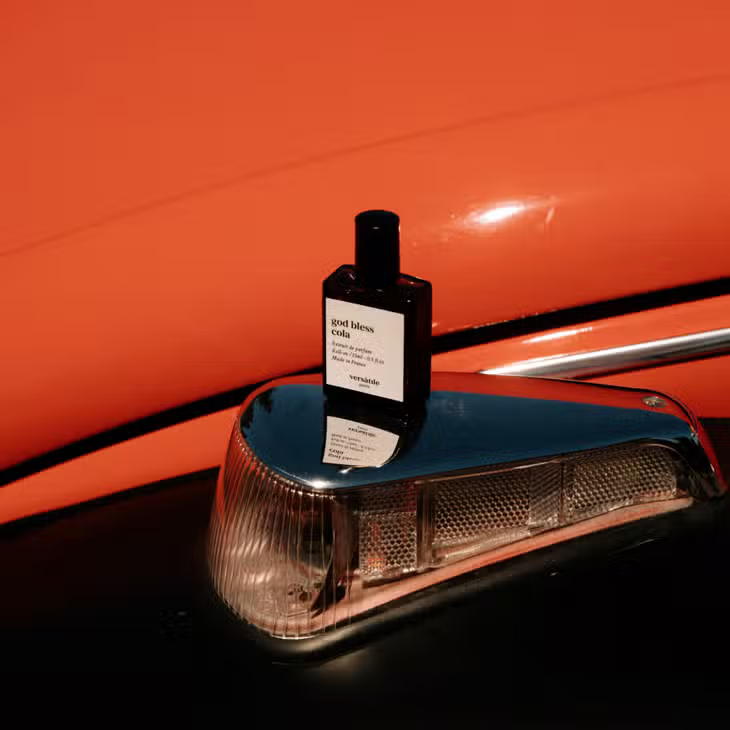 God Bless Cola Roll-on Parfümöl in einer dunklen Glasflasche mit schwarzem Deckel vor orangem Hintergrund, Duftöl.