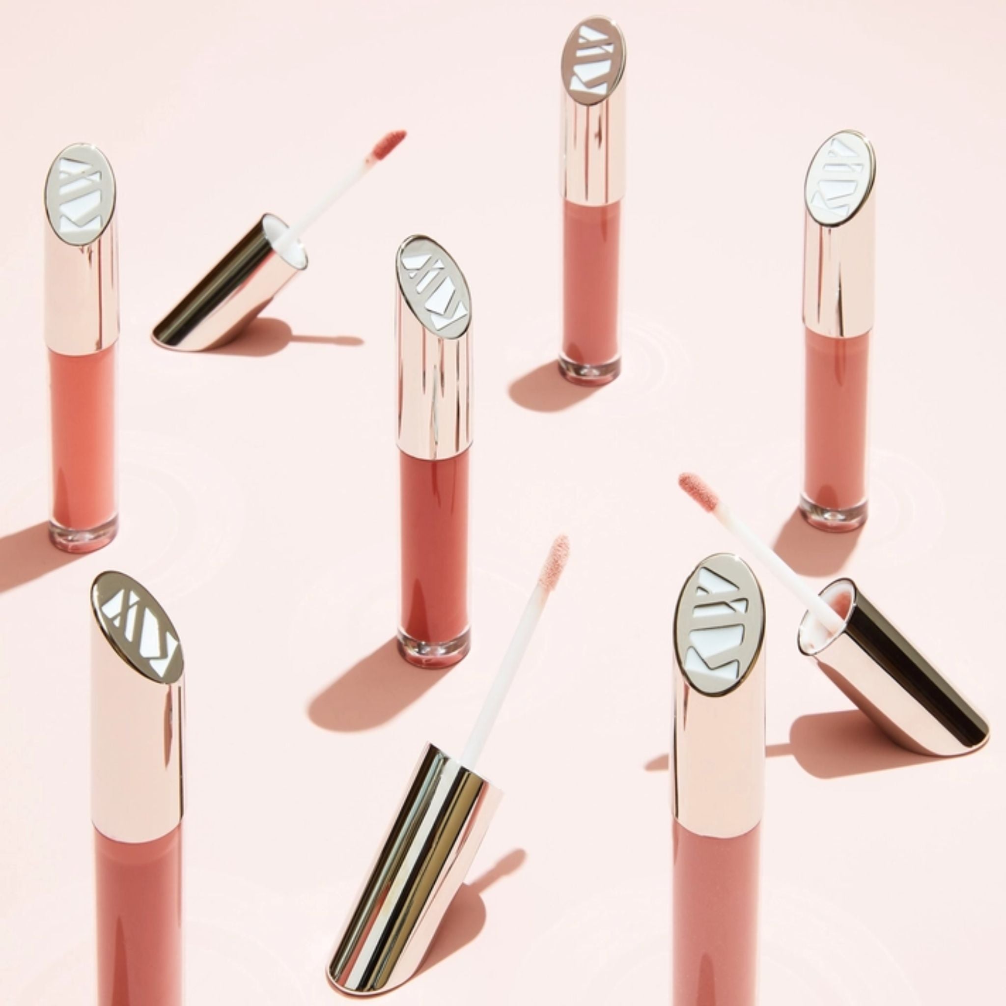 Multiple Lip Gloss Fascination glass tubes with silver caps on a pink background, glossy makeup.