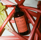 L:A Bruket No. 339 Hand & Body Wash, braune Flasche, rotes Etikett, umgeben von Rabarber