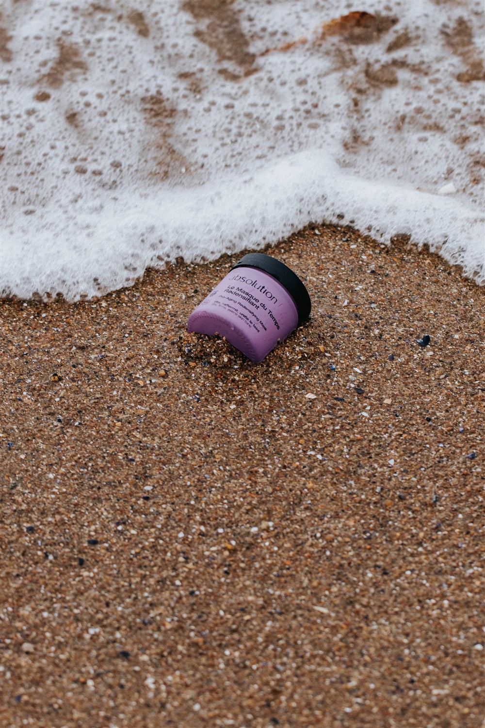 Insolution Le Masque du Temps Redensifiant purple jar with black lid on sand, skin care