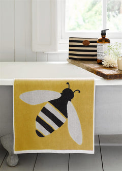 Buzzy Bee Organic Cotton Washcloth – yellow with bee design, white border, on bathtub – skin care