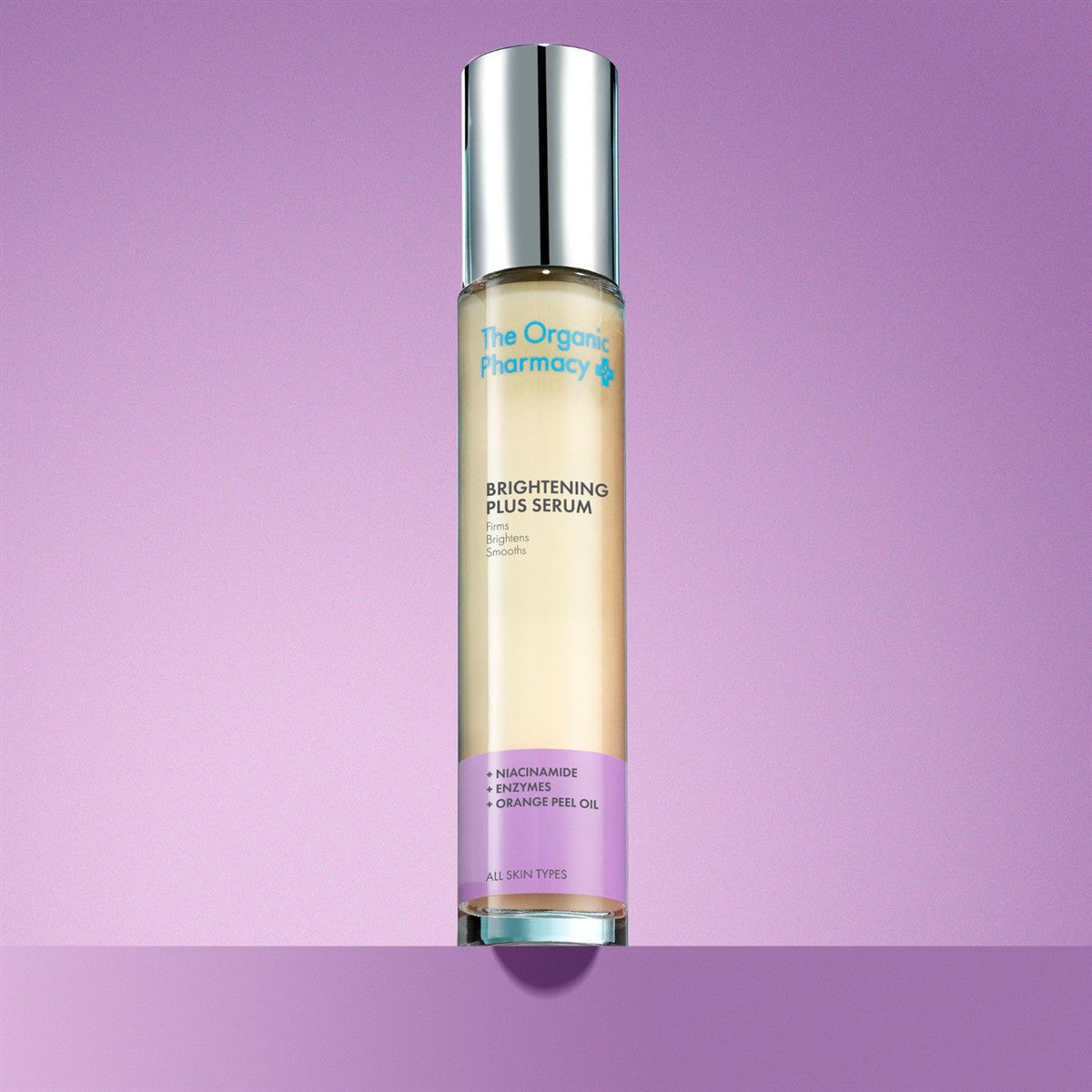 The Organic Pharmacy Brightening Plus Serum in a bottle with silver cap on a purple background, skin care mood