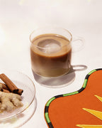 Chai Koffee – durchsichtige Tasse mit braunem Getränk, Eiswürfel, Zimtstangen und Ingwer im Hintergrund – Getränke