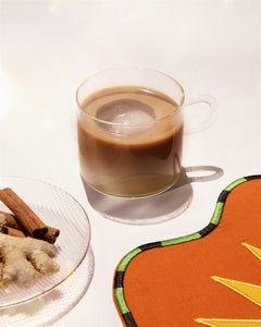 Chai Koffee – clear mug with brown drink, ice cube, cinnamon sticks and ginger in background – beverages
