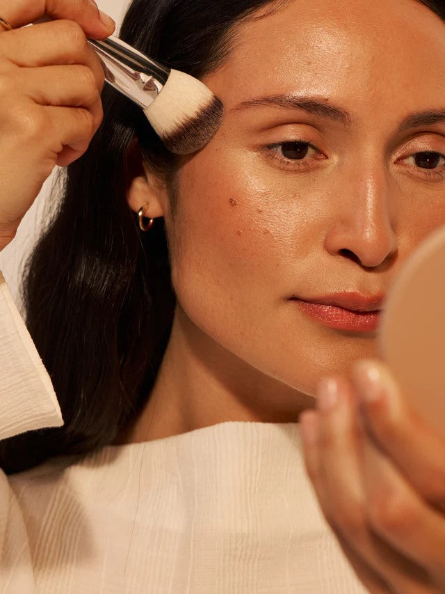 Person nutzt Sculpting Brush für ein präzises Make-up auf hellem Hintergrund, Gesichtskonturierung.
