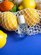 Esprit de Contradiction Eau de Parfum – klares Glasfläschchen mit weißem Sprühkopf, blauer Hintergrund, Zitrusfrüchte – Parfüm
