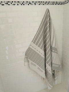Biarritz Grey striped grey and white towel against a white tiled wall, bath accessory