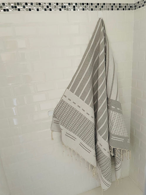 Biarritz Grey gestreiftes Handtuch in Grau und Weiß vor weißer Fliesenwand, Badzubehör