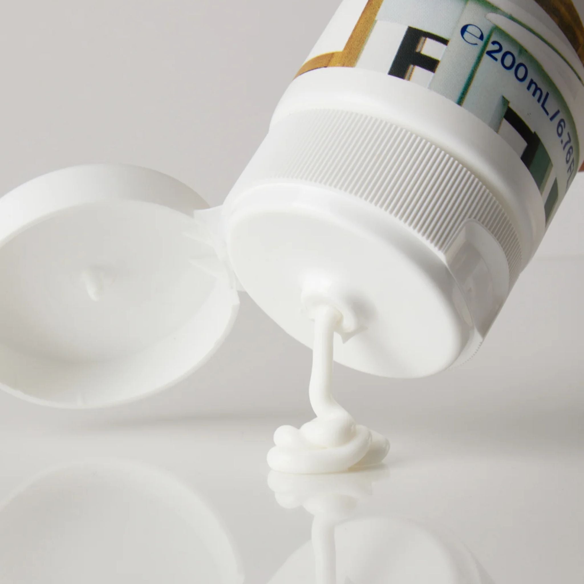 Körpermilch in einer weißer Tube mit offenem Deckel auf weißem Hintergrund, Hautpflege