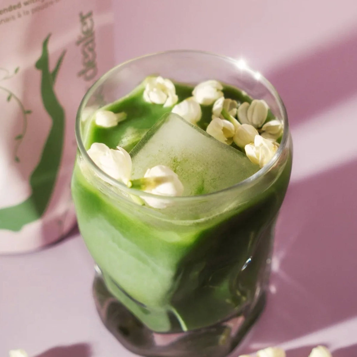 Jasmine Matcha in einem Glas auf rosa Hintergrund, grünes Getränk mit Blüten