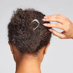 Metal French Hair Pin Silber im lockigen Haar vor grauem Hintergrund, elegantes Haar-Accessoire