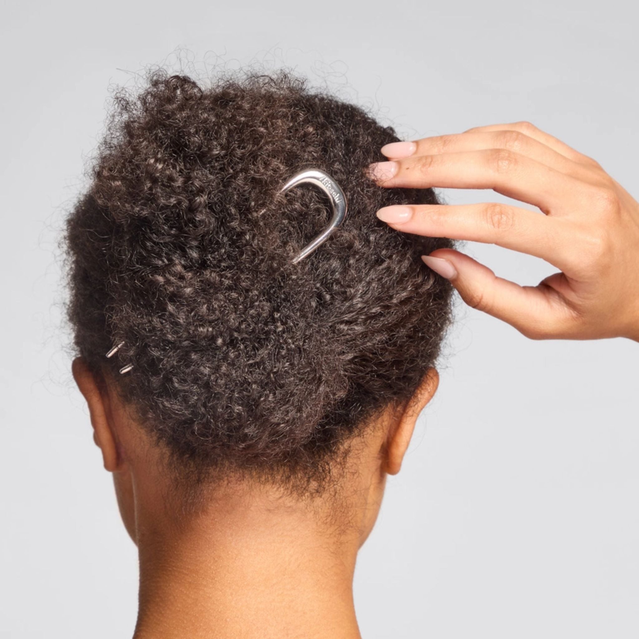 Metal French Hair Pin Silber im lockigen Haar vor grauem Hintergrund, elegantes Haar-Accessoire
