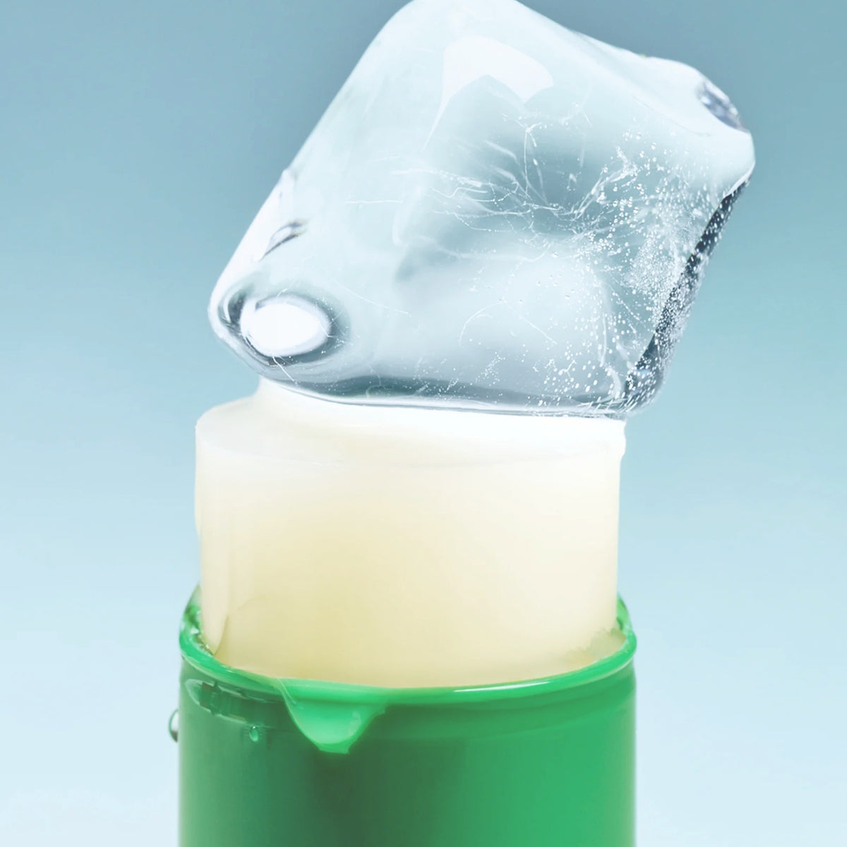SHOT Koffein-Augenserum-Stick: Ein Stück Eis liegt auf dem ausgefahrenen, cremefarbenen Serum-Stick in einem grünen Gehäuse.