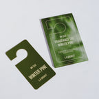 L:A Bruket No. 342 Fragrance Tag Winter Pine: ein dunkelgrüner Duftanhänger neben seiner Kartenverpackung.